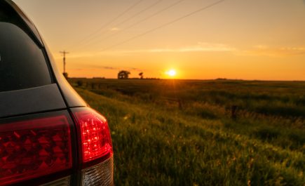 Looking past the tail lights on a car at the sunset over a farm field.